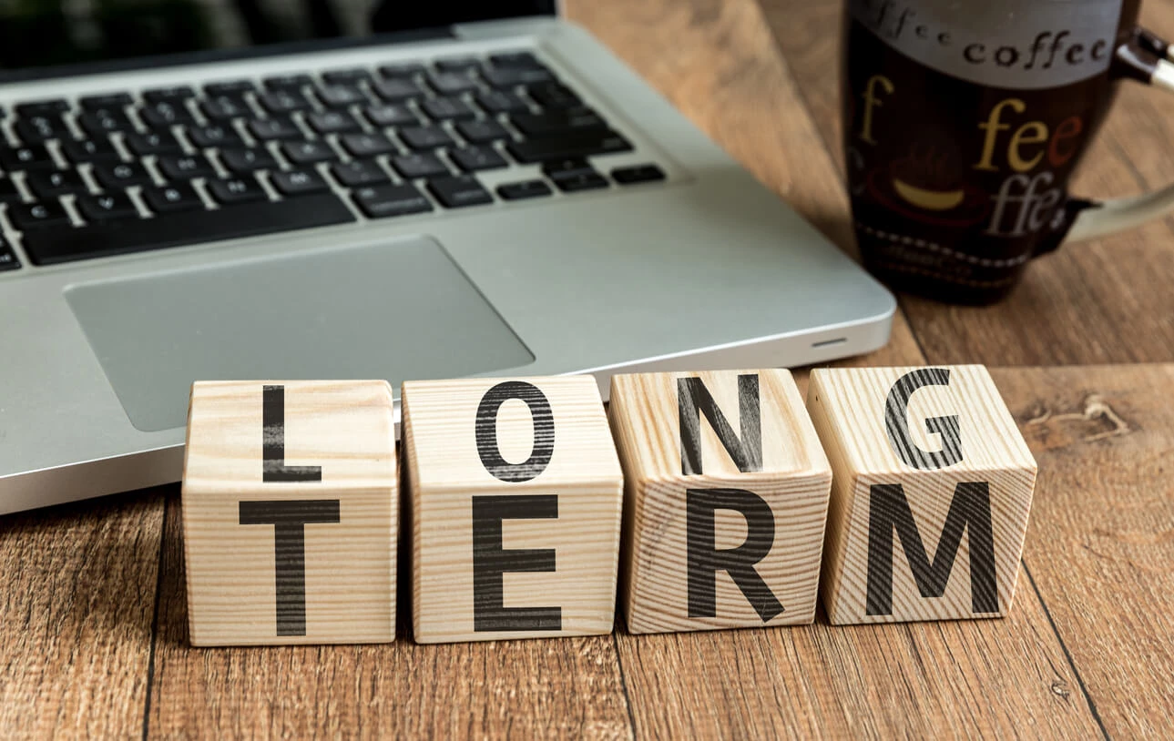 Desk features laptop computer, coffee mug, and wooden block spelling out long term