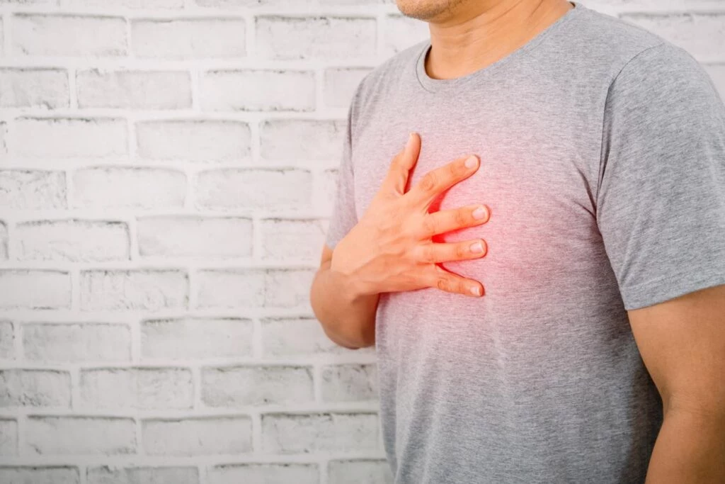 White man wearing gray t-shirt holds his right hand to his chest in pain