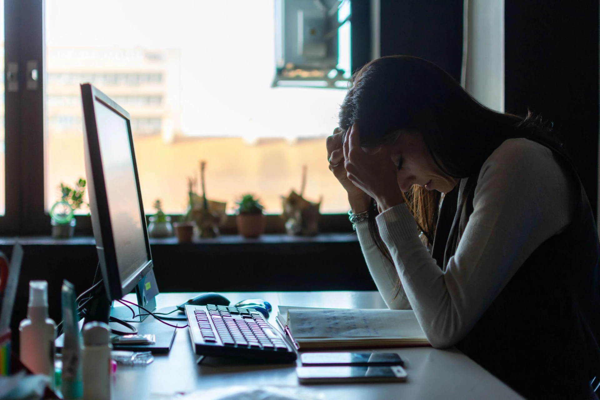 Frustrated women sits at her desk as she holds her head in her hands